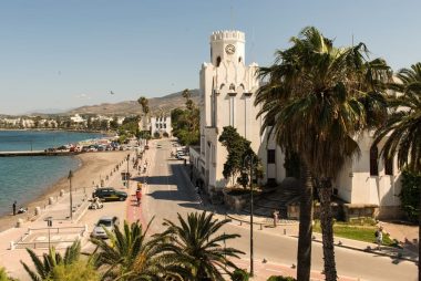 Charming street view of Kos, Greece with palm trees and historic architecture under a bright summer sky.